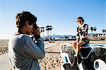 Young woman sitting on wall, young man photographing her with camera