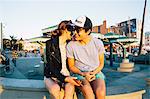 Romantic young couple sitting on wall at coast, Venice Beach, California, USA