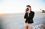 Young woman photographing with instant camera on beach, Venice Beach, California, USA