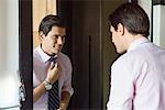 Man looking in mirror, adjusting necktie