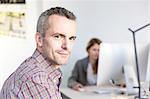 Side view of mature man in office looking at camera smiling