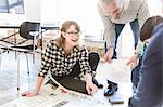 Architects on office floor discussing blueprint smiling