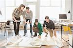 Architects discussing blueprints on wooden floor