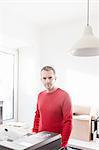 Mature man in office wearing red sweater looking at camera smiling