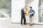 Architect holding rolled up blueprints talking to homeowners at front door