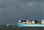Container ship entering Rotterdam harbour with help of tug boat