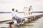 Group of friends on pier, female friends walking towards male friends sitting on edge of pier