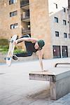 Young male skateboarder doing balance skateboard trick on urban concourse seat