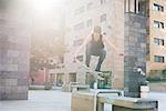 Young male skateboarder jumping over urban concourse seat