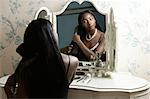 Young woman sitting at dressing table, looking in mirror, brushing hair