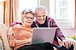 Senior couple on living room sofa looking at laptop