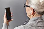 Over shoulder view of gray haired woman wearing ear buds holding smartphone