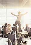 Colleagues watching exuberant businessman celebrating on top of desks in office