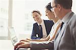 Smiling business people using laptop in conference room