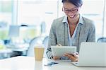 Smiling businesswoman using digital tablet with coffee in office