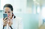 Smiling businesswoman using cell phone in office corridor
