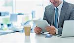 Smiling businessman using digital tablet with coffee in office