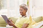 Mature women using digital tablet eating popcorn on sofa