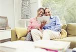 Smiling mature couple using digital tablet on living room sofa