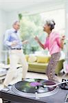 Playful nature couple dancing in living room behind record player