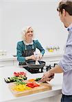 Smiling couple slicing and cooking vegetables in kitchen