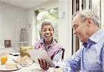 Mature couple laughing and using digital tablet at breakfast table