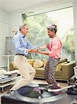 Playful mature couple dancing behind record player in living room