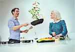 Surprised couple cooking flipping vegetables in skillet in kitchen