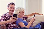 Couple texting with cell phones on living room sofa