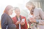 Women texting and drinking coffee outdoors