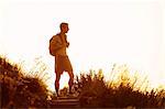 Bare chested male hiker with backpack on trail at sunset