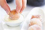 close-up of person's hand dipping fresh beignet in sauce, traditional new orleans or french cuisine