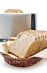 Wholemeal toast bread slices placed on a cotton cloth napkin in a wicker basket close up arranged with electric toaster isolated on white background.
