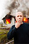 Man smoking cigarette in front of burning building