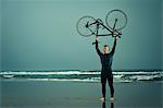 Man wearing wetsuit holding bicycle on beach