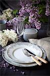 Lilacs in vase and plates on table, close-up