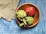 Overhead View of Pomegranate and Artichokes in Wooden Bowl on Blue Tablecloth