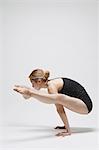 Attractive young Japanese woman wearing black pants and tank top practicing yoga on white background