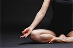 Attractive young Japanese woman wearing black pants and tank top practicing yoga on black background