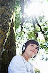 Boy in headphones leaning against tree