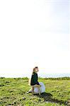 Girl sitting alone in field under bright sky