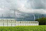 Greenhouses, pylons and wind turbines under cloudy sky