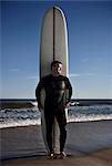 Portrait of mature man standing with tall surfboard on beach