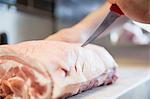 Close up of butchers hand scoring meat joint in butchers shop