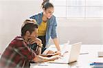 Creative young business people working at laptop in sunny office