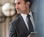 Pensive corporate businessman with digital tablet looking away