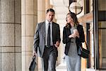 Corporate businessman and businesswoman with coffee walking and talking in cloister