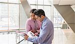 Corporate businessmen reviewing paperwork in modern office lobby