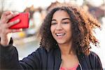 Beautiful happy mixed race African American young woman girl teenager female child smiling with perfect teeth taking selfie photograph with red cell phone