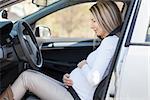 Young pregnant woman behind the steering wheel having contractions